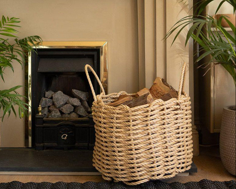 A handwoven rope runner and a basket made from natural fibers, placed on wood flooring in front of homely fireplace.