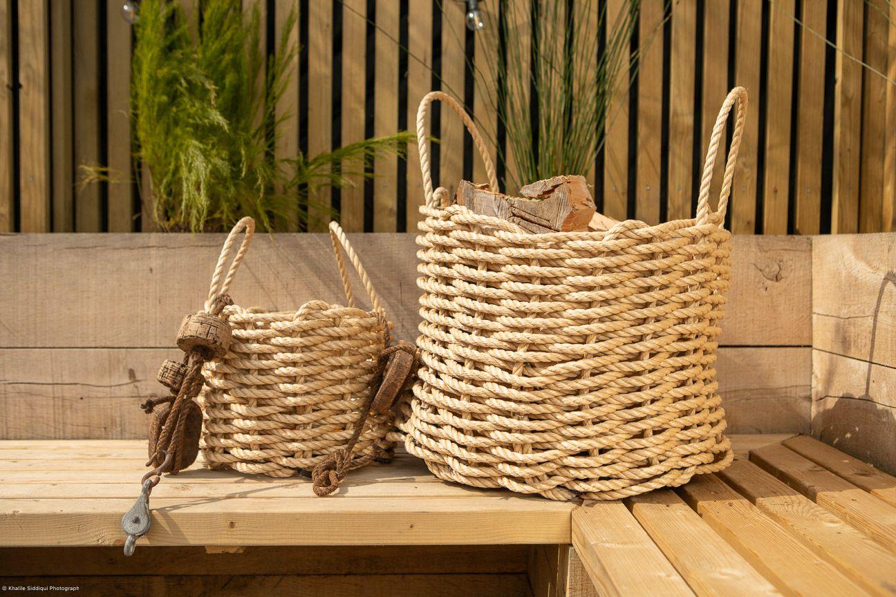 Two handwoven medium-sized baskets made of sisal with a removable plywood base, placed on a wooden surface, one larger and one smaller with a Cornish flag decorative element attached to the smaller one.